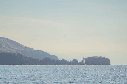 A sailboat passing distant headlands and sea stacks